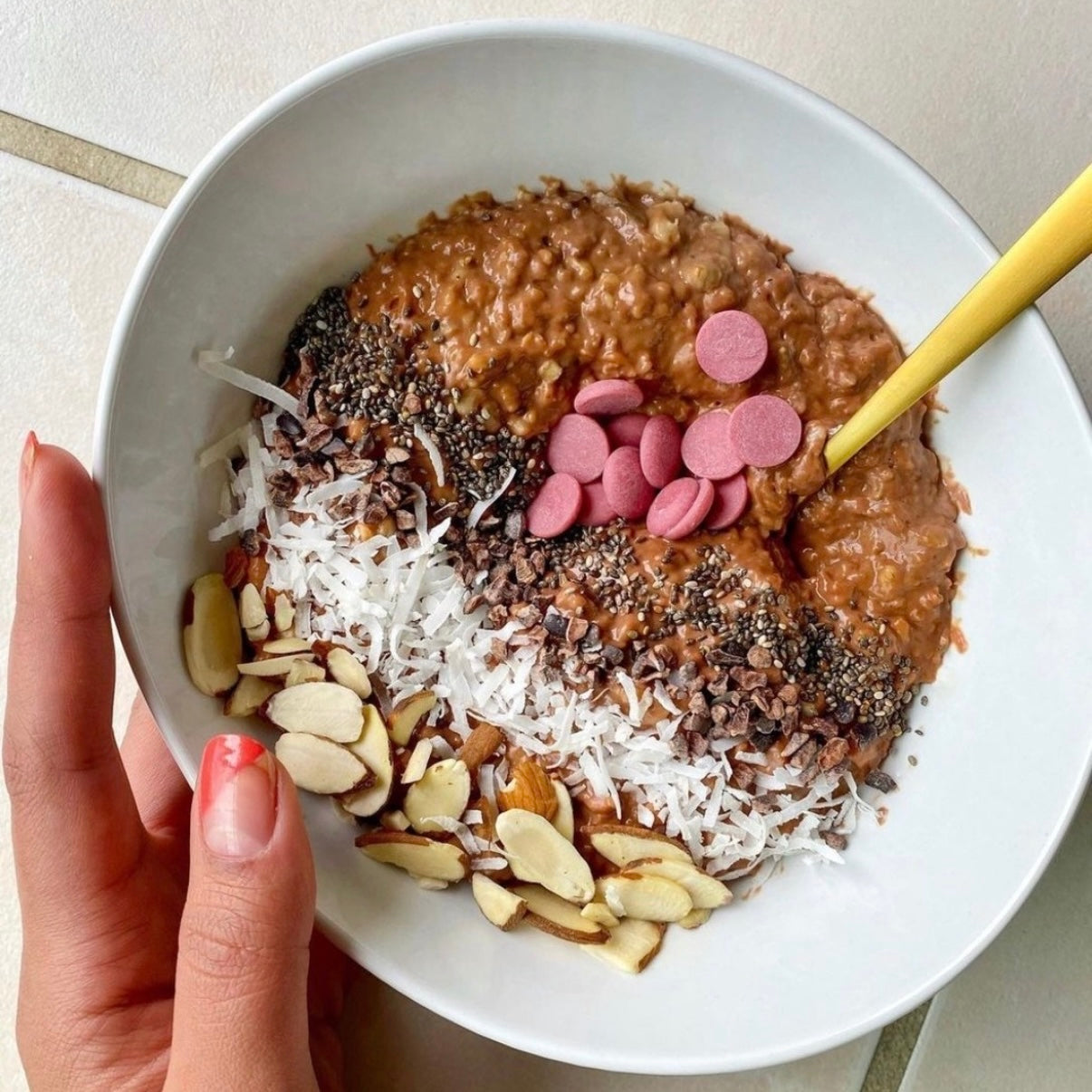 A person holding a spoon above a bowl of overnight oats with chia seeds, ready to serve or eat the warm breakfast dish.